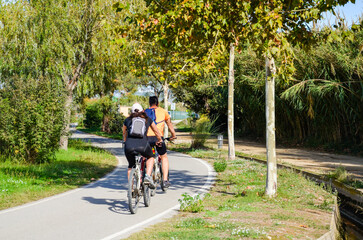 Young couple, man and woman, play sports by riding a bicycle through a public circuit with trees in nature