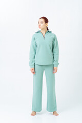 Woman with red hair in a warm, comfortable turquoise sports suit stands barefoot and looks away....