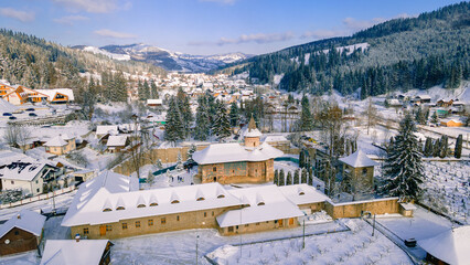 Aerial photography of Voronet Monastery, located in Suceava county, Romania in winter, sunny day with snow. Photo was shot from a drone at a lower altitude revealing the beautifull mountain background