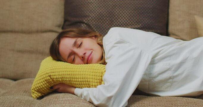 Calm young caucasian woman lying down on couch pillow in living room to relax, take nap. Tired girl rest on sofa at home