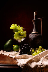 Butelka, wino oraz kiść winogron na czerwonym tle. Martwa natura z owocami winogron i Avokado, w tle limonka i cytryna. Tekstura jako tapeta na pulpit. Białe i czerwone winogrona.