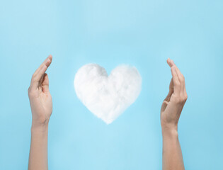 Levitating white white heart shaped cloud guarded by hands in blue sky