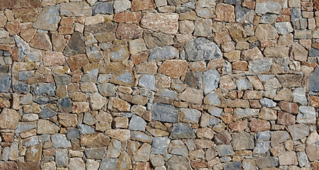 Rustic exterior wall made from brown flat natural stones of different sizes arranged randomly. Background and texture