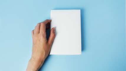 A mockup of an close book in womans hand isolated on blue .mockup with shadow. book endpaper. Blank catalog, magazines or brochure.