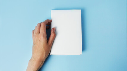 Obraz premium A mockup of an close book in womans hand isolated on blue .mockup with shadow. book endpaper. Blank catalog, magazines or brochure.