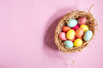 Easter eggs in nest with yellow straw. Very colorful and happy concept. Placed on a pink background. Happy easter 