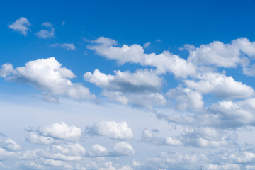 A skyscape with cumulus clouds in white and grey and a clear deep blue sky in the summer