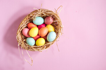 Easter eggs in nest with yellow straw. Very colorful and happy concept. Placed on a pink background. Happy easter 