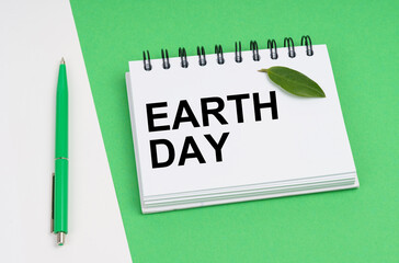 On a white-green background lies a pen, a leaf of a plant and a notepad with the inscription - earth day