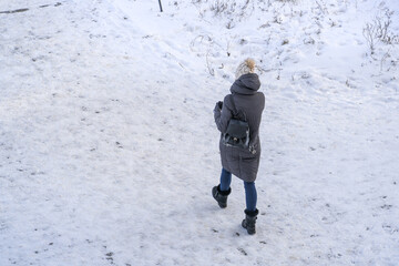 A lonely girl walks along a snowy road on a winter day in the city