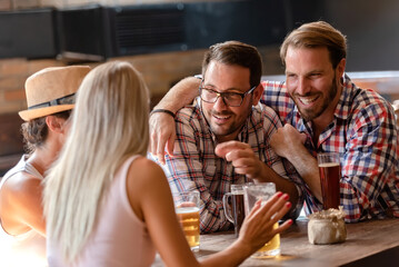 Young couples drinking beer and laughing together at the bar. Happy friends having fun at bar -...