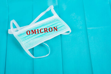 Medical mask on a green background with the inscription Omicron, isolated, coronavirus concept (COVID-19). Up close.