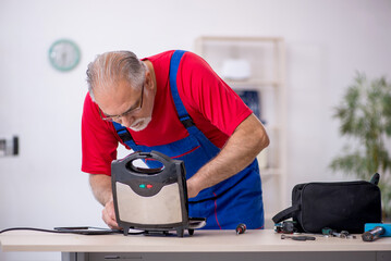 Old repairman repairing sandwich maker at workshop