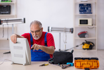 Old repairman repairing heater at workshop