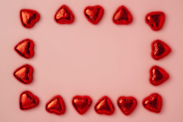 A frame of many shiny heart-shaped candies wrapped in foil on a pink background