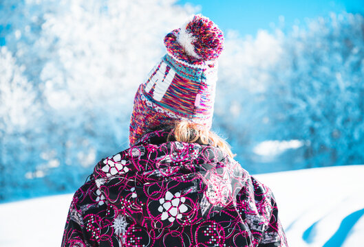 Girl hiker stands in front of a winter trees looking to the snowy landscape. Rear view.