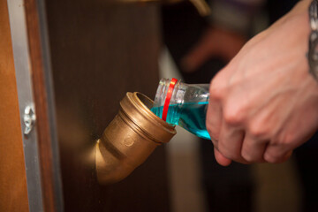 A man pours blue water from a bottle into a pipe.