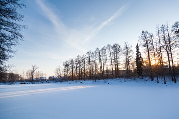 Fototapeta premium Frozen pond under a large layer of snow on the background of sunset.