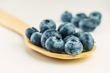 Close up view of several fresh blueberries in a wooden spoon.