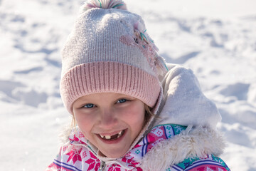 portrait of a little cheerful girl 7-8 years old in winter, against the backdrop of snow