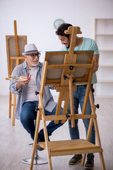 Old painter teaching young student at studio