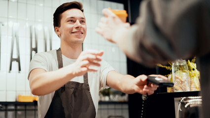 Male barista waiter employee in uniform in a cafe selling takeaway coffee