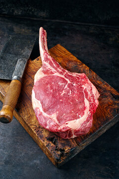 Raw dry aged chianina tomahawk steak offered as close-up with a cleaver on old rustic wooden board