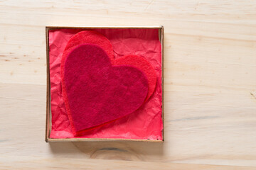two felt hearts inside a box with crumpled red paper on wood with blank space