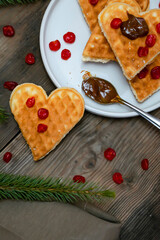 Homemade Belgian waffles heart shaped on plate with colorful red sweet cherry berries, banana, and boiled condensed milk, dessert food. background for Valentines day, womens day, love, romance