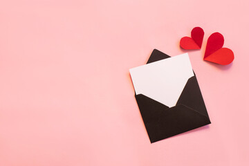 Black paper envelope with blank white note mockup inside and Valentines hearts on pink background. Flat lay, top view. Romantic love letter for Valentine's day concept