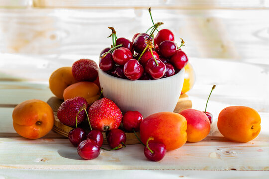 Fresh, juicy fruits, strawberries and nectarines on the table, cherries in a traditional wooden bowl, photographed in warm light