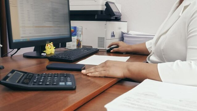 Businesswoman in white formal suit starts her working day in the office by checking email. Side view of hand scrolling computer mouse wheel.