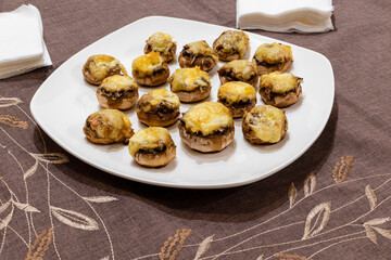 Appetising baked champignon mushrooms with cheese top on a white plate on the dining table
