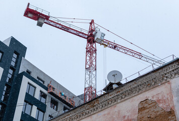 Fototapeta premium Construction crane on background of old and new houses and gray sky with light snowfall