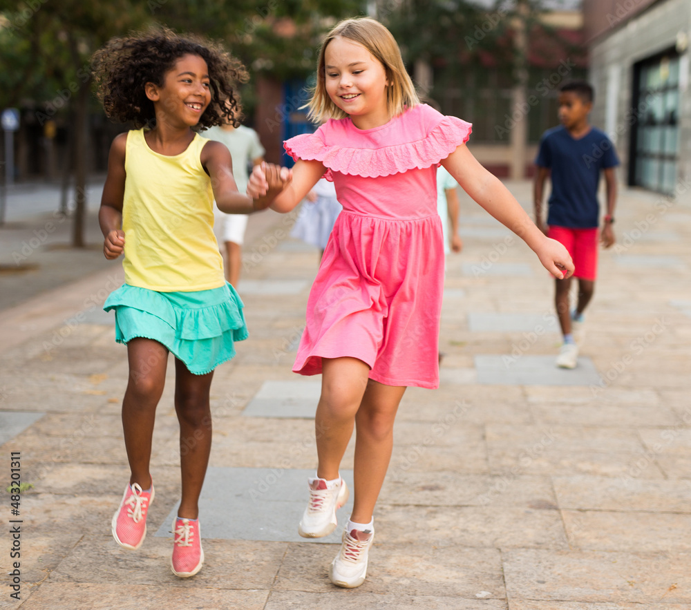 Wall mural happy blonde preteen girl enjoying walk with african american girl friend along city street on summe