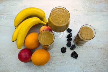 Fruit smoothie in glasses, with fruits on the table.