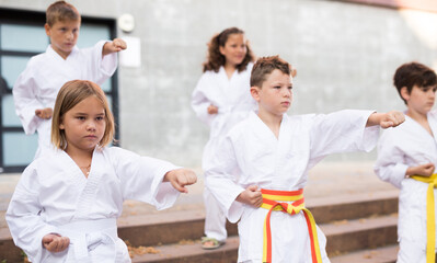 Positive children wearing white sports uniform practicing karate on a street near school