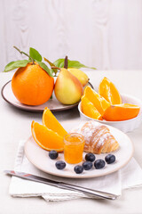 Breakfast with a fresh croissant , jam and ripe blueberries and juicy oranges, pears on a white table, vertical