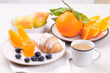 Breakfast with a cup of coffee, fresh croissant , ripe blueberries and juicy oranges on a white background