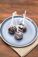 Delicious Chocolate cake pops decorated white sprinkles on plate on napkin, wooden background, pastry, desserts on stick with tape. Tasty food. copy space