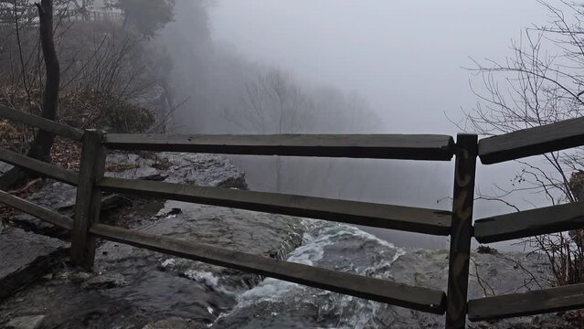 Waterfall under fence over cliff into fog Thatcher Park NY