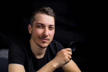 Young handsome man and a magnifying glass on black background in low key. Search symbol....