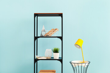 Shelf unit with decor and table with lamp near color wall
