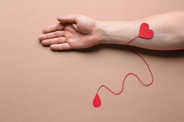 Male hand, red paper heart and drop of blood on color background. Donation concept
