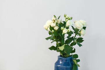 Vase with bouquet of beautiful fresh roses near grey wall, closeup