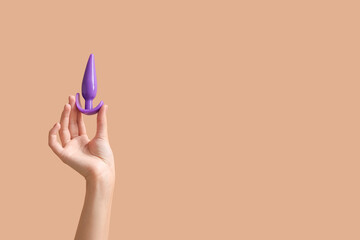 Female hand with anal plug sex toy on color background