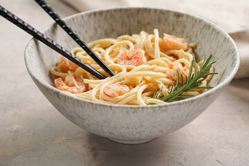 Deep grey japanese style bowl with pasta spaghetti with heavy cream and roasted shrimps with garlic sauce and parmesan cheese, black chopsticks on grey concrete surface
