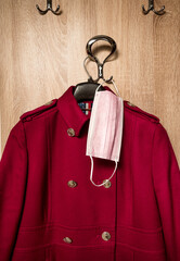 Red womans coat and Protective surgical face mask on anteroom coat hanger stand during covid-19 pandemics