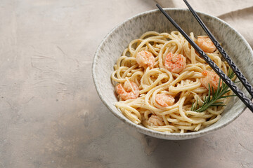 Deep grey japanese style bowl with pasta spaghetti with heavy cream and roasted shrimps with garlic sauce and parmesan cheese, black chopsticks on grey concrete surface
