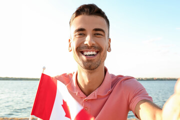 Young man with flag of Canada taking selfie near river